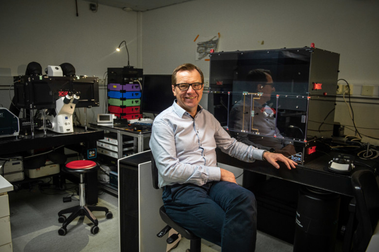 Hymyilevä, vaaleakauluspaitainen mies istuu suurikokoisen, tumman mikroskooppilaitteen äärellä Turun Biotiedekeskuksen laboratoriossa.